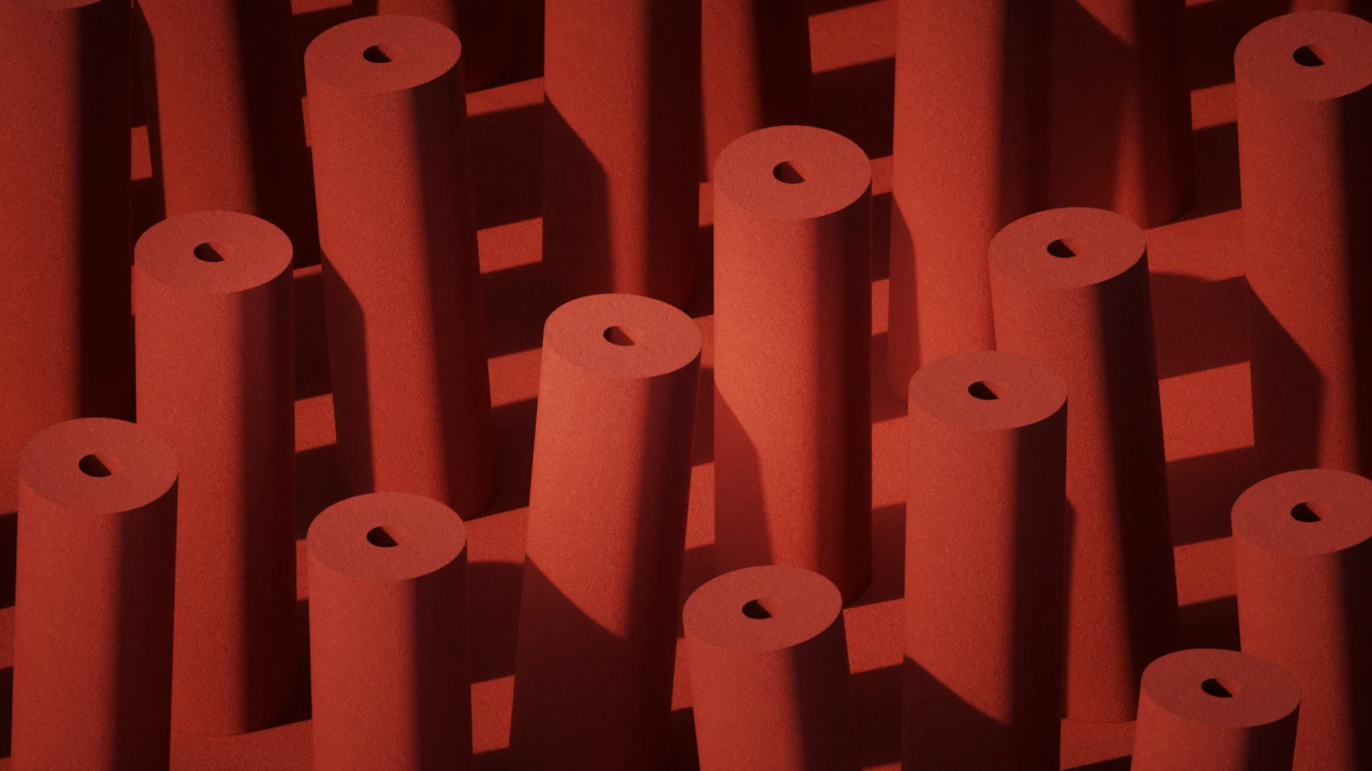 Rows of upright terracotta cylinders of varying heights on a sandy surface, each casting a sharp diagonal shadow